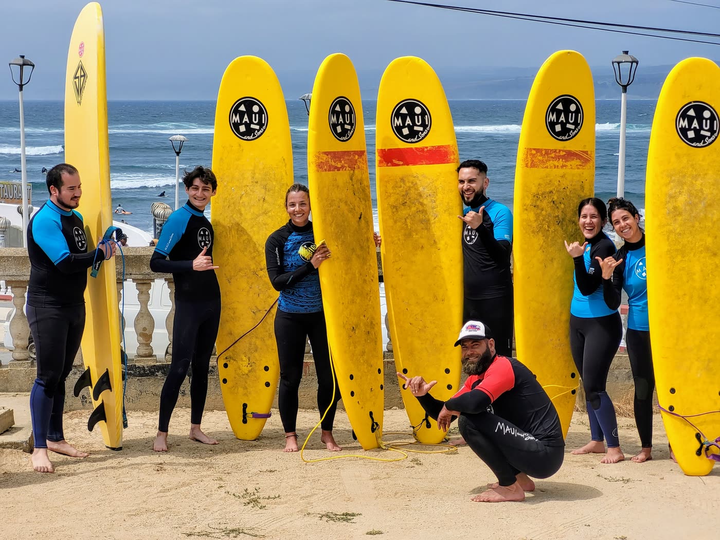 Grupo de alumnos con tablas de surf amarillas frente a la playa